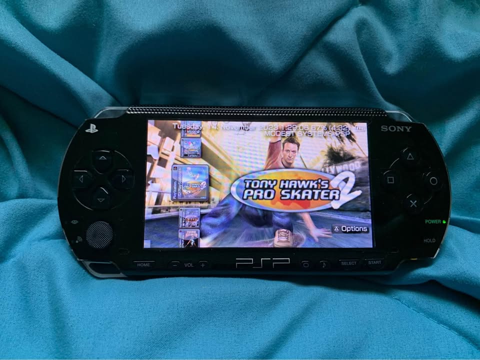 Modded PSP 1000 with 128GB storage card and charger cable showing preloaded 7000+ retro games Dayviewer and Cheats plug-in